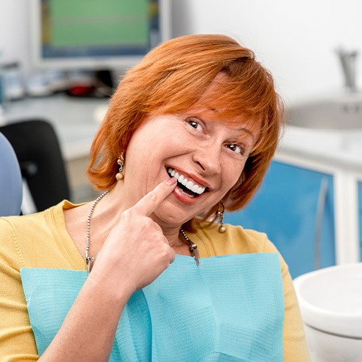 A senior woman pointing to the new dental implant she received