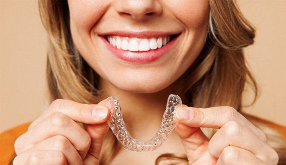 Smiling patient holding clear aligner