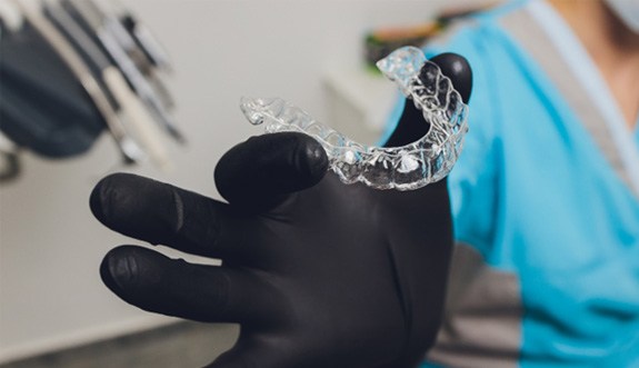 Dentist holding clear aligner with black gloves