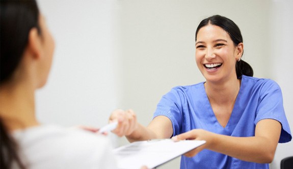 Dental assistant smiling while handing patient form